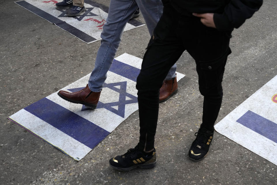 People walk on representations of the Israeli flag at the scene Wednesday's bomb explosion in the city of Kerman about 510 miles (820 kms) southeast of the capital Tehran, Iran, Thursday, Jan. 4, 2024. Investigators believe suicide bombers likely carried out an attack on a commemoration for an Iranian general slain in a 2020 U.S. drone strike, state media reported Thursday, as Iran grappled with its worst mass-casualty attack in decades and as the wider Mideast remains on edge. (AP Photo/Vahid Salemi)