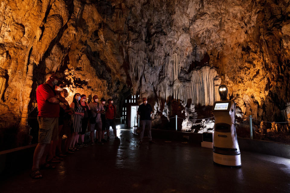 Persephone guides the visitors inside Alistrati cave, about 135 kilometers (84 miles) northeast of Thessaloniki, Greece, Monday, Aug. 2, 2021. Persephone, billed as the world's first robot used as a tour guide inside a cave, has been welcoming visitors to the Alistrati cave, since mid-July. (AP Photo/Giannis Papanikos)