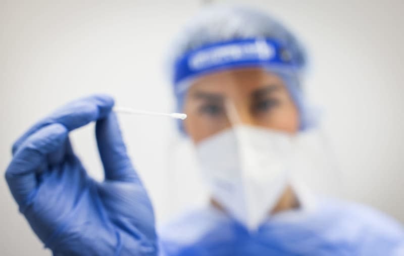 An employee at EcoCare's Corona Test Center in the Tango Terminal at Hamburg Airport holds a test stick for a nasopharyngeal swab. A planned international accord on how to limit deaths and coordinate international action during a pandemic is in the balance ahead of talks at the World Health Organization (WHO). Christian Charisius/dpa