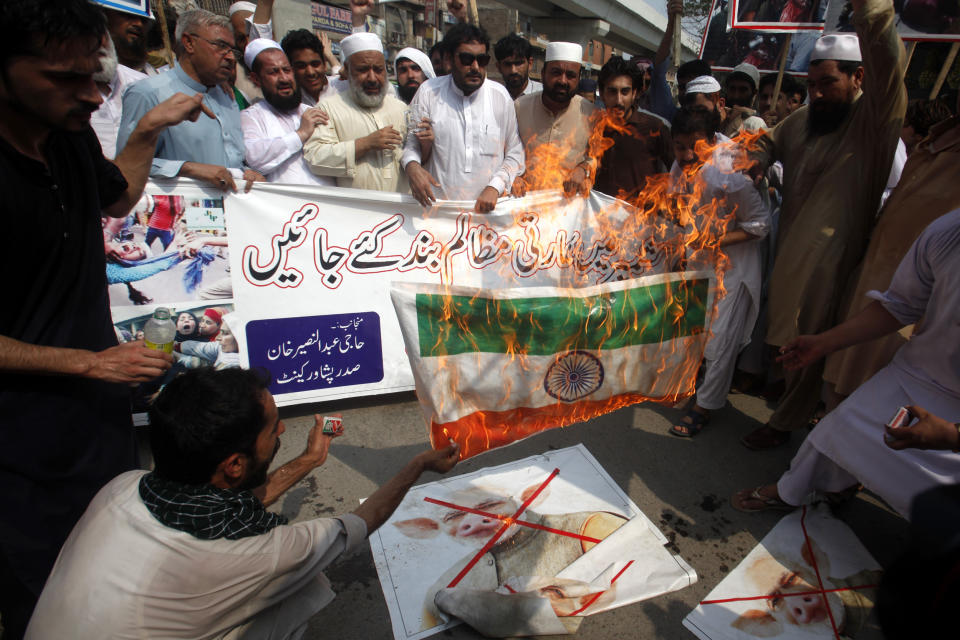 Pakistani protesters burn posters showing Indian Prime Minister Narendra Mody and a representation of an Indian flag during a rally in Peshawar, Pakistan, Tuesday, Aug. 6, 2019. Pakistan President Arif Alvi convened his country's parliament to discuss India's surprise actions on Kashmir. Banner reads "stop atrocities in Indian Kashmir." (AP Photo/Muhammad Sajjad)