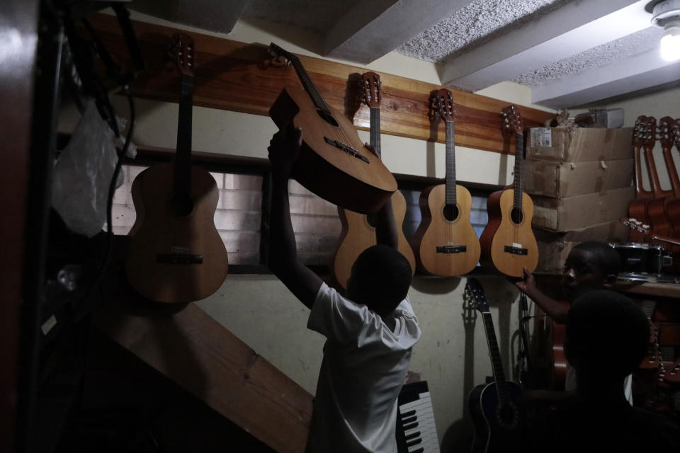 Music students hangs guitars back up after practice at the Plezi Mizik Composition Futures School in Port-au-Prince, Haiti, Thursday, Sept. 21, 2023. Across the capital, hundreds of children are playing percussion, piano and bass guitar to drown out the violence and hunger around them. (AP Photo/Odelyn Joseph)
