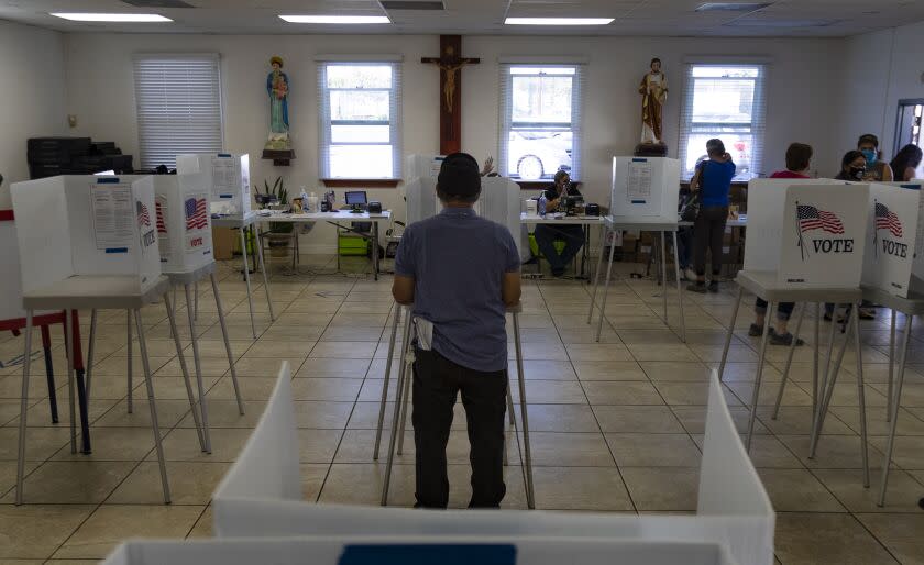 FONTANA, CA - NOVEMBER 3, 2020: A voter fills out his ballot with Christ on the crucifix hanging on the wall inside the recreation center at St. Joseph's Catholic Church on Election Day on November 3, 2020 in Fontana, California. (Gina Ferazzi / Los Angeles Times)