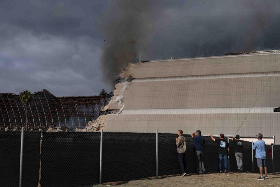 Spectators watch as a historic blimp hangar burns in Tustin, Calif., Tuesday, Nov. 7, 2023. A fire destroyed a massive World War II-era wooden hangar that was built to house military blimps based in Southern California. (AP Photo/Jae C. Hong)