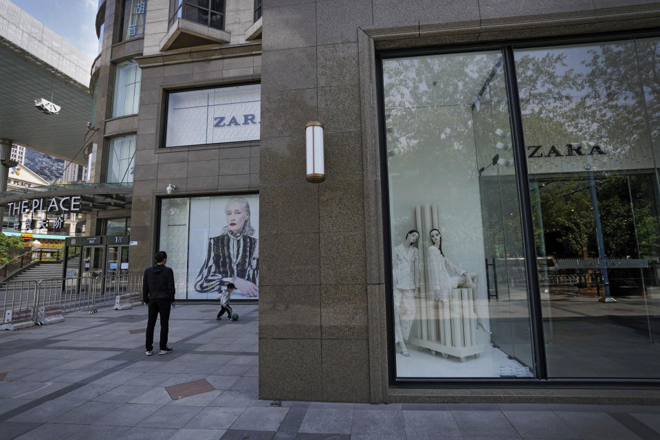 A man plays with a child near a shuttered ZARA flagship store on Thursday, May 12, 2022, in Beijing. China's leaders are struggling to reverse an economic slump without giving up anti-virus tactics that shut down Shanghai and other cities, adding to challenges for President Xi Jinping as he tries to extend his time in power. (AP Photo/Andy Wong)