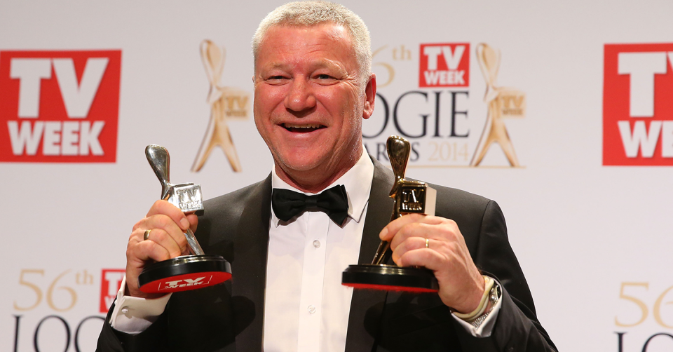 Scott Cam smiles as he holds up a gold and silver Logie award in front of TV Week media wall.