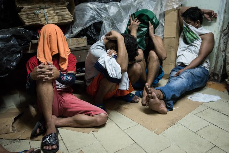 Alleged drug suspects cover their faces during a drug raid in Manila, Philippines.