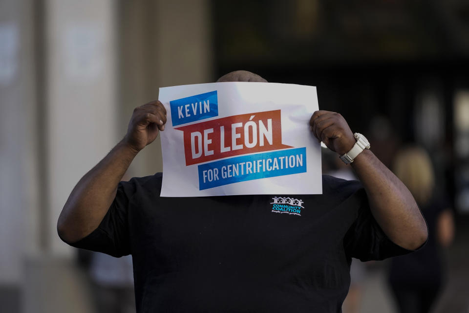 A protester covers his face with a sign mocking city councilmen Kevin de León outside the Los Angeles City Hall in Los Angeles, Tuesday, Oct. 18, 2022. The demonstrators demanded the city council stop its virtual meeting Tuesday until two of its members resign over racist remarks. (AP Photo/Jae C. Hong)