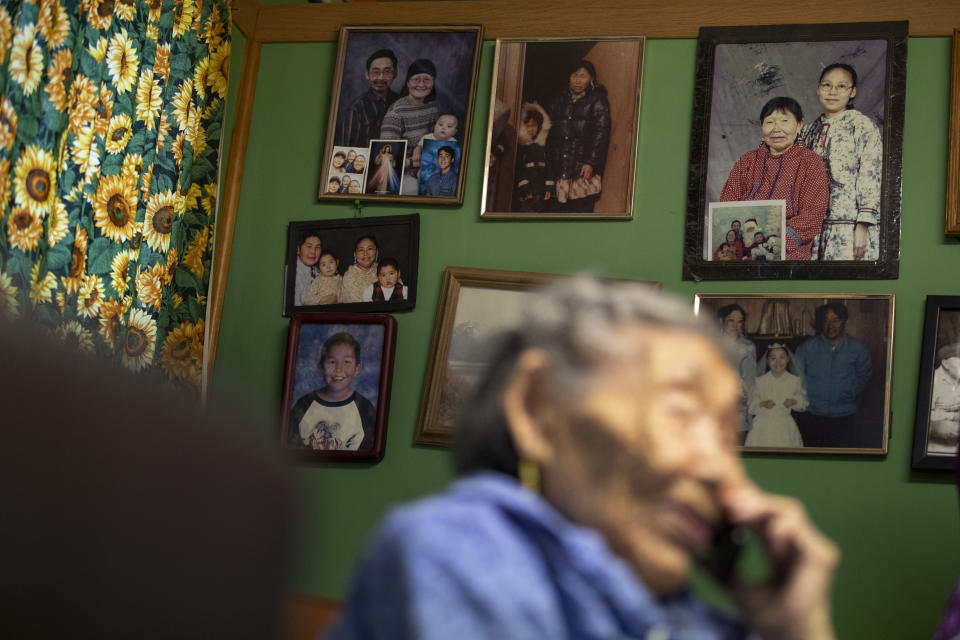 In this Monday, Jan. 20, 2020 image, family pictures hang on the wall as Lizzie Chimiugak talks on the phone at her home in Toksook Bay, Alaska. Chimiugak, who turned 90 years old on Monday, is scheduled to be the first person counted in the 2020 U.S. Census on Tuesday. (AP Photo/Gregory Bull)