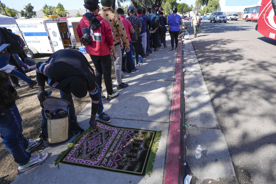 A migrant picks up his rug after prayer as he waits for a bus to the airport Friday, Oct. 6, 2023, in San Diego. San Diego's well-oiled system of migrant shelters is being tested like never before as U.S. Customs and Border Protection releases migrants to the streets of California's second-largest city because shelters are full. (AP Photo/Gregory Bull)