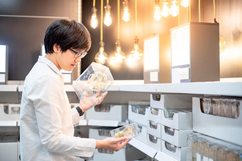 Young Asian man choosing package of electrical light bulb, furniture home decoration shopping concept