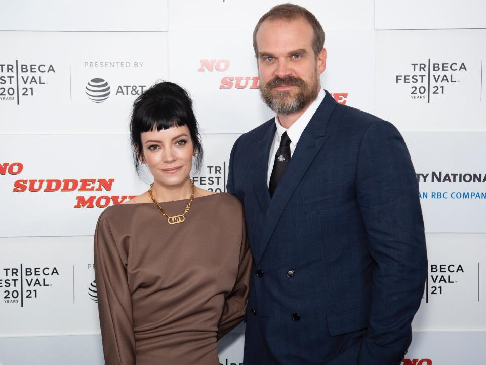 Lily Allen, in a brown dress and gold necklace, poses for photos with David Harbour, in a navy suit, on the red carpet in 2021.