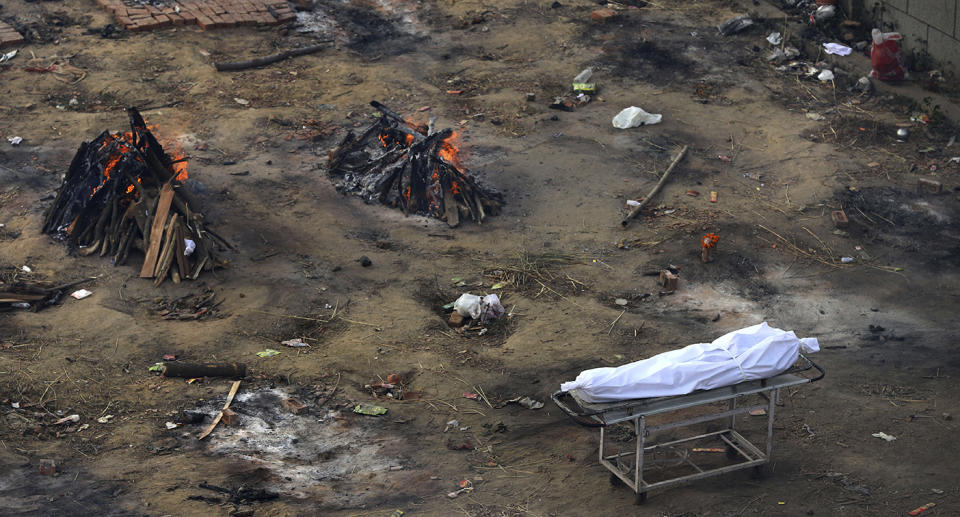 A dead body waits to be cremated as multiple funeral pyres of those who died of COVID-19 burn at a ground that has been converted into a crematorium for mass cremation of coronavirus victims, in New Delhi, India, Wednesday, April 21, 2021. Delhi has been cremating so many bodies of coronavirus victims that authorities are getting requests to start cutting down trees in city parks, as a second record surge has brought India's tattered healthcare system to its knees.Â (AP Photo)