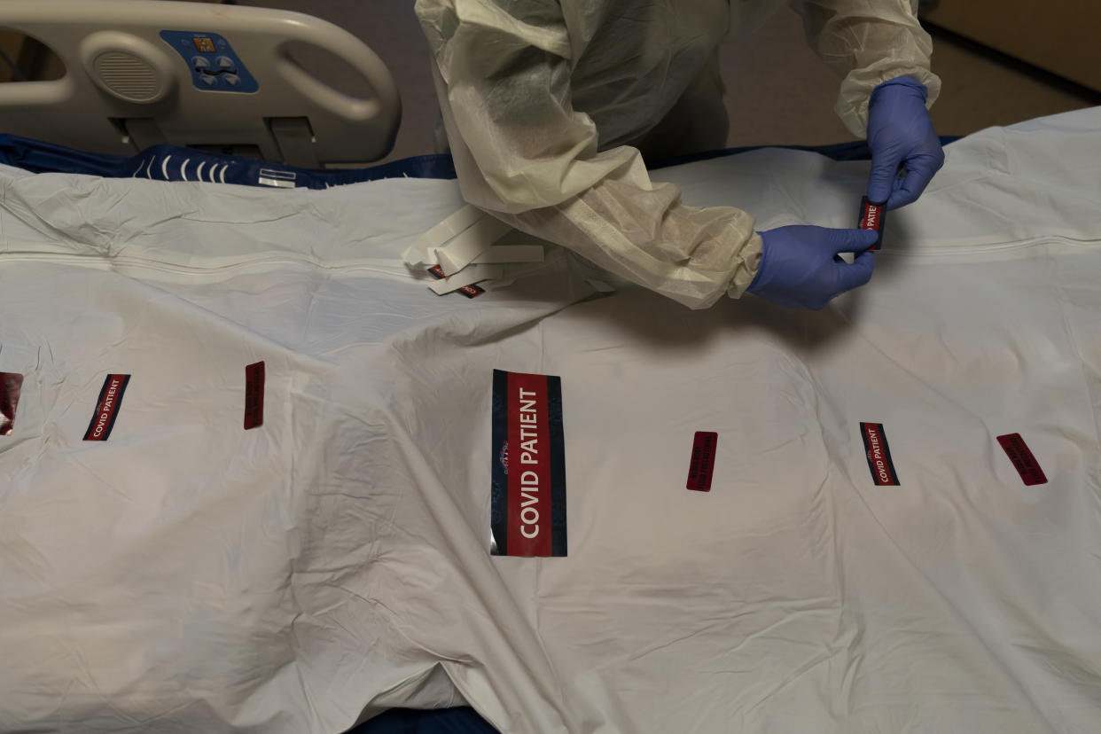 Registered nurse Bryan Hofilena attaches "COVID Patient" stickers on a body bag of a patient who died of coronavirus at Providence Holy Cross Medical Center in Los Angeles, Tuesday, Dec. 14, 2021. Many hospitals across the country are struggling to cope with burnout among doctors, nurses and other workers. Already buffeted by a crush of patients from the ongoing surge of the coronavirus's delta variant, they're now bracing for the fallout of another highly transmissible mutation. (AP Photo/Jae C. Hong)