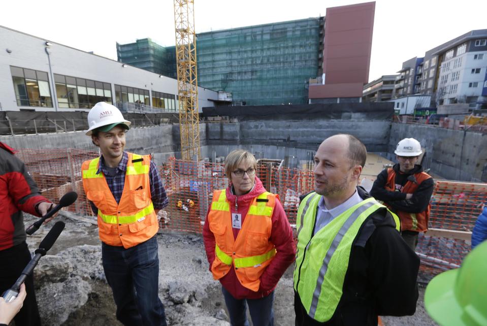 Julie Stein, center, University of Washington's Burke Museum executive director, addresses media members with Christian Sidor, left, the museum's curator of vertebrate paleontology, and Scott Koppelman, builder Amli Residential vice president, above the site where a fossilized mammoth tusk was found earlier in the week Thursday, Feb. 13, 2014, in Seattle. In the crowded south Lake Union neighborhood where Amazon.com workers go out for espresso, an ice age mammoth died 10,000 years ago and remained until this week, when a plumbing contractor crew uncovered its tusk. Paleontologists with the Burke Museum are working with the building contractor to remove the tusk. (AP Photo/Elaine Thompson)