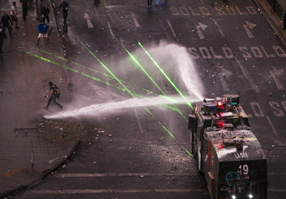 Police water cannon advances on anti-government demonstrators during protest in Santiago, Chile, Monday, Nov. 4, 2019. Thousands of Chileans took to the streets again Monday to demand better social services, some clashing with police, as protesters demanded an end to economic inequality even as the government announced that weeks of demonstrations are hurting the country's economic growth. (AP Photo/Esteban Felix)
