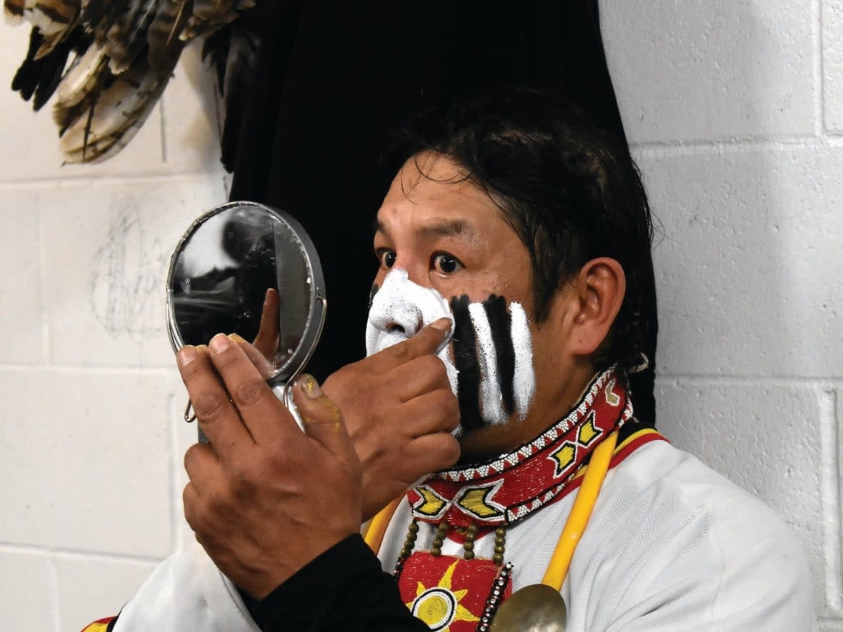 Harry Buffalocalf, a player from Nekaneet First Nation, applies face paint in between the second and third period of the Battle of the Little Big Puck in 2020. The Cree team dons traditional wear, including headdresses, animal hide and face paint, while the opposing team wears cowboy hats and chaps. (Marcus Day/Maple Creek News - image credit)