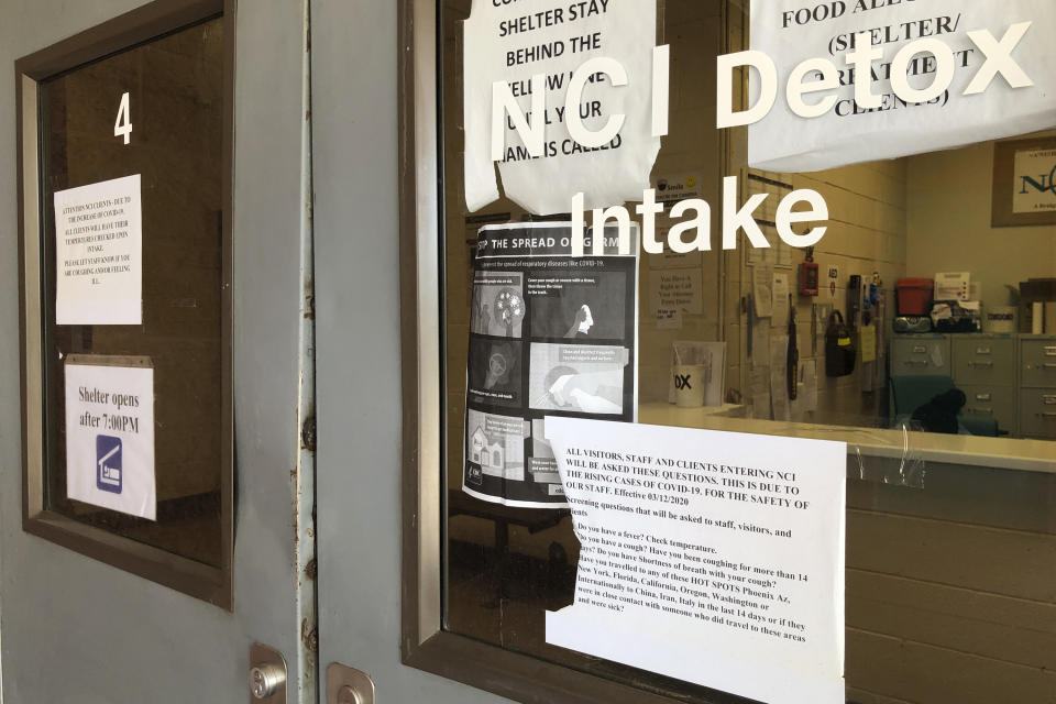 In this May 7, 2020, photo signs hang on doors at the Na'Nizhoozhi Center detox facility in Gallup, N.M. A night of revelry before bars and restaurants shut in New Mexico appears to have led to an outbreak in the detox center and homeless shelter on the fringes of the Navajo Nation. (AP Photo/Morgan Lee)