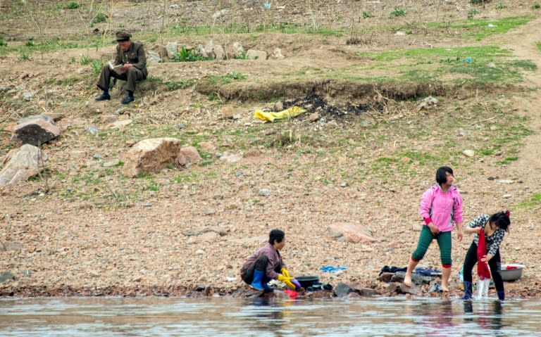 A North Korean soldier reads a book near women washing clothes in the Yalu border river on April 16, 2017