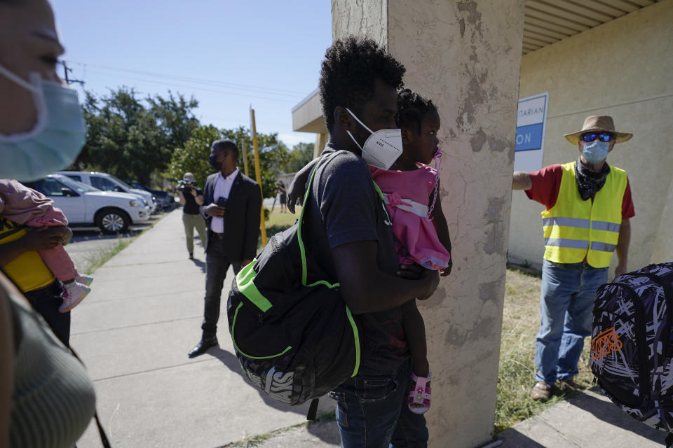 Dave, right, who declined to give his last name, from Toledo, Ohio, wears a neon vest as migrants are released from U.S. Customs and Border Protection custody, Friday, Sept. 24, 2021, in Del Rio, Texas. Dave, who has been to Haiti many times, befriended a woman named Ruth, who he believes is still in custody after she crossed the Rio Grande with her husband and their 3-year-old daughter. Dave drove down from Ohio to Southwest Texas in hopes of picking the family up and driving them to Ohio, where Ruth has family awaiting them. (AP Photo/Julio Cortez)