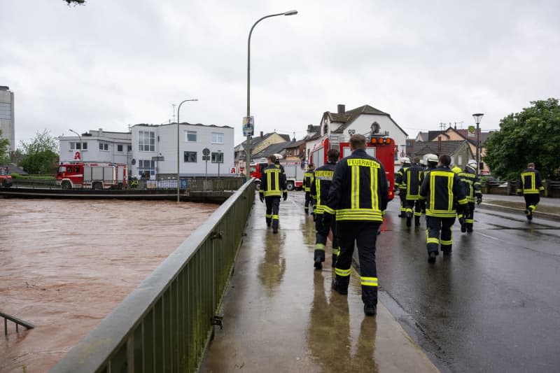Firefighters walk across a bridge under which the flooding river Theel flows. Harald Tittel/dpa