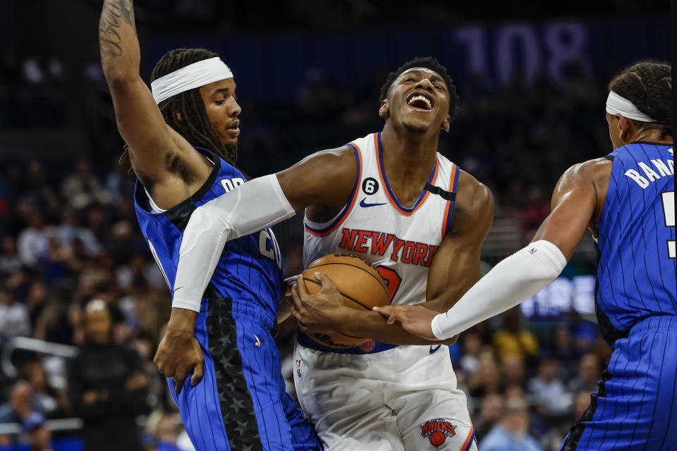 New York Knicks guard RJ Barrett, center, pushes through defenders Orlando Magic forward Paolo Banchero, right, and guard Markelle Fultz, left, during the first half of an NBA basketball game, Thursday, March 23, 2023, in Orlando, Fla. (AP Photo/Kevin Kolczynski)