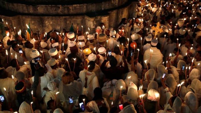 Ethiopian orthodox Christians in a crowd holding candles on the roof of the Church of the Holy Sepulchre in Jerusalem. It is dark and they are wearing white.