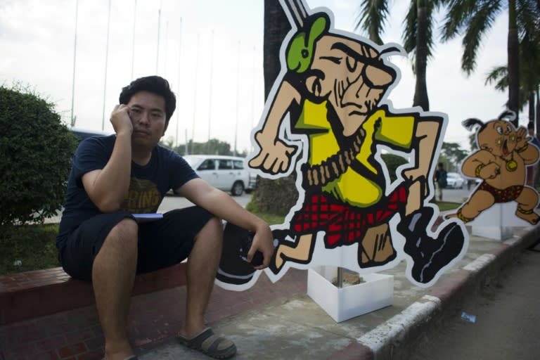 A man sits next to Myanmar's famous cartoon posters at an exhibition in Yangon marking one hundred years of political cartoons