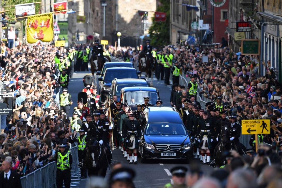 Members of the public gather to watch the procession of Queen Elizabeth II's coffin, from the Palace of Holyroodhouse to St Giles Cathedral, on the Royal Mile on September 12, 2022, where Queen Elizabeth II will lie at rest. - Mourners will on Monday get the first opportunity to pay respects before the coffin of Queen Elizabeth II, as it lies in an Edinburgh cathedral where King Charles III will preside over a vigil. (Photo by ANDY BUCHANAN / AFP) (Photo by ANDY BUCHANAN/AFP via Getty Images)