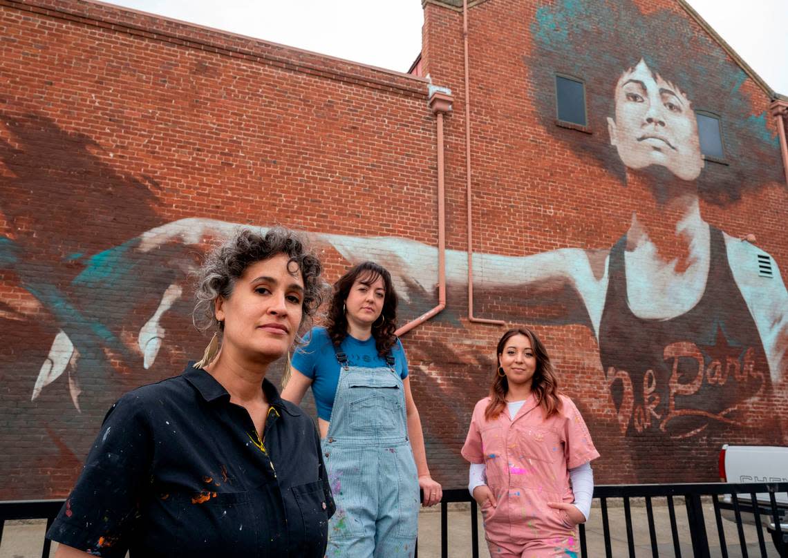 Sacramento artists, Jaya King, left, Jolene Rose Russell, center, and Uli Smith stand in front of a mural March 22 titled “Guild Goddess,” painted by King in 2018 on Oak Park’s Guild Theater for Wide Open Walls. They claim Wide Open Walls exploits new artists by underpaying them.