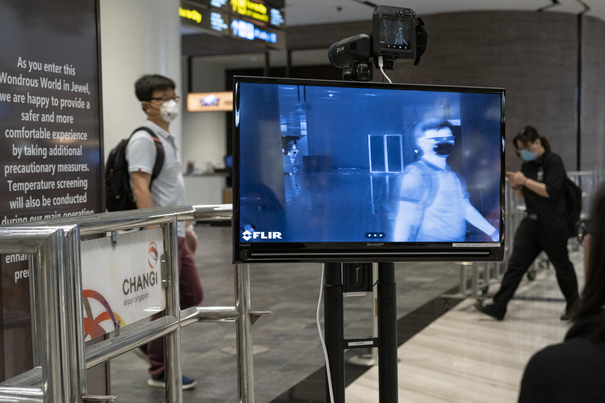 People wearing masks walk past a temperature screening area at Terminal 1 of Changi Airport on 22 March, 2020, in Singapore. (PHOTO: Getty Images)