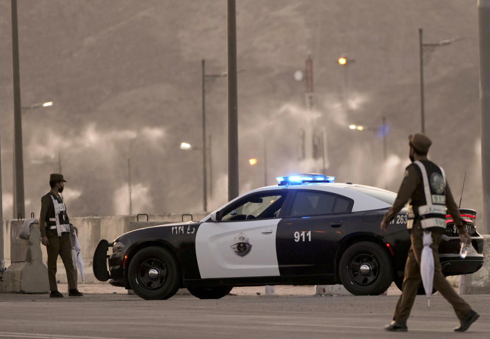 Water mist is sprayed as Saudi policemen stand alert at a check point in the Arafat tent camp, in the Saudi Arabia's holy city of Mecca, Tuesday, July 5, 2022. Saudi Arabia is expected to receive one million Muslims to attend Hajj pilgrimage, which will begin on July 7, after two years of limiting the numbers because coronavirus pandemic. (AP Photo/Amr Nabil)