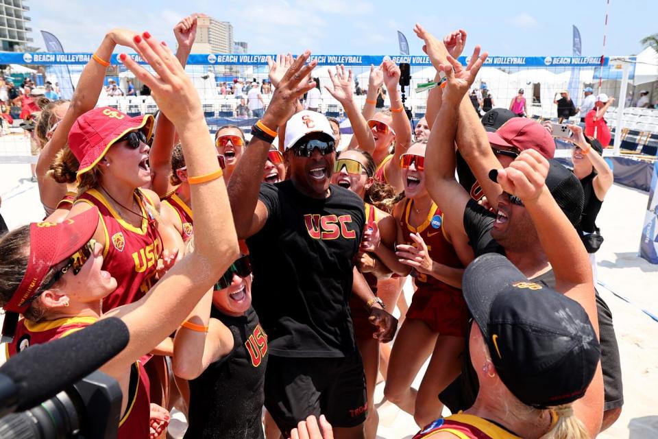 USC coach Dain Blanton is surrounded by players celebrating winning the Trojans' fourth straight beach volleyball title.