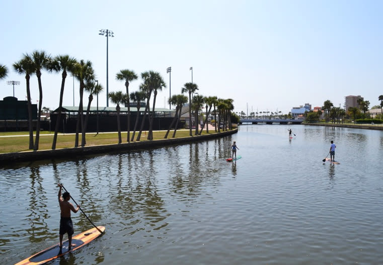 This March 22, 2011 photo provided by Three Brothers Boards shows Austin Marvin and tour customers passing the Jackie Robinson Memorial Ball Park on the Halifax River, Daytona Beach, Fla. A sort of combination between surfing and kayaking, standup paddling has exploded in popularity the past few years. It's relatively easy and can be done just about anywhere there's water. (AP Photo/Three Brothers Boards, Justin Murray)