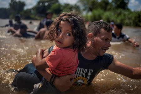 FILE PHOTO: Luis Acosta helps carry 5-year-old Angel Jesus, both from Honduras, as a caravan of migrants from Central America en route to the United States crossed through the Suchiate River into Mexico from Guatemala in the outskirts of Tapachula, Mexico, October 29, 2018. A second caravan of migrants bound for the U.S. border waded through the Suchiate River into Mexico after they clashes with Mexican police at the border bridge. Dozens were injured and one was killed by a rubber bullet. REUTERS/Adrees Latif/File Photo