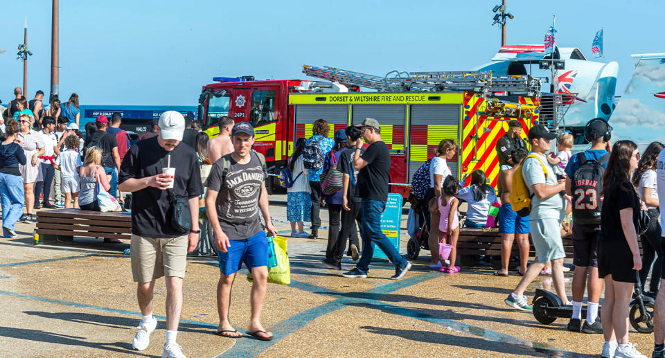 Crowd of people at the beach standing in front of a firetruck. 