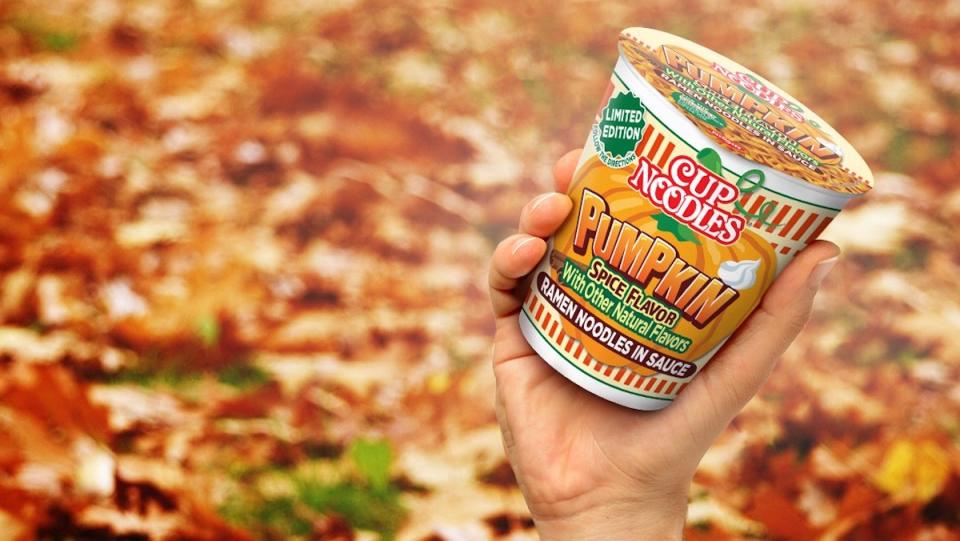 A hand holding a serving of Cup Noodles comes up from a leaf covered ground weird news