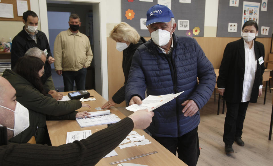 A member of the electoral commission gives ballots to a man at a polling station in Skopje, North Macedonia, on Sunday, Oct. 31, 2021. North Macedonia is holding a runoff of local elections on Sunday seen as key test for the leftist government after center-right opposition has won mayoral posts in 21 municipalities compared with only nine of ruling Social-democrats in the first round of the vote two weeks ago. (AP Photo/Boris Grdanoski)