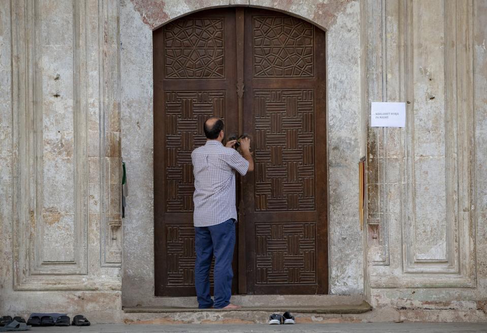 An employee of the Kosovo Islamic Community closes the door of the Sultan Mehmet Fatih mosque in Pristina, Kosovo, Friday, July 31, 2020. Government measures banned all public gatherings including religious due to fear of recent uprise in COVID-19 cases. (AP Photo/Visar Kryeziu)