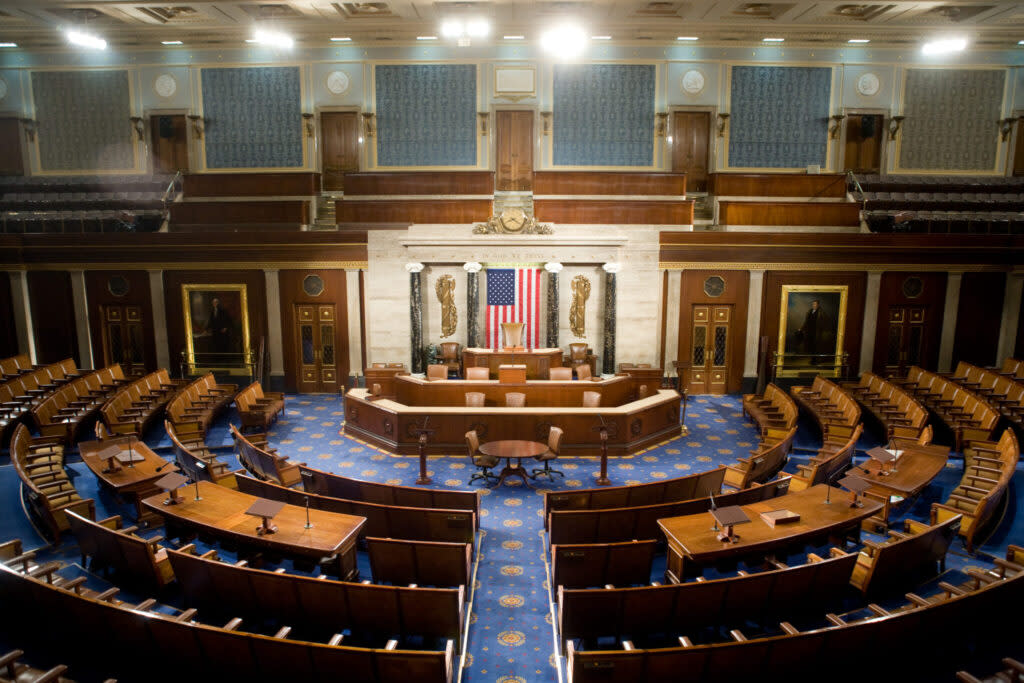 The empty chamber of the U.S. House of Representatives. Framed paintings of George Washington and the Marquis de Lafayette falnk the rostrum