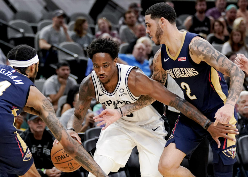 San Antonio Spurs' DeMar DeRozan, center, drives between New Orleans Pelicans' Brandon Ingram, left, and Lonzo Ball during the second half of an NBA preseason basketball game, Sunday, Oct. 13, 2019, in San Antonio. (AP Photo/Darren Abate)