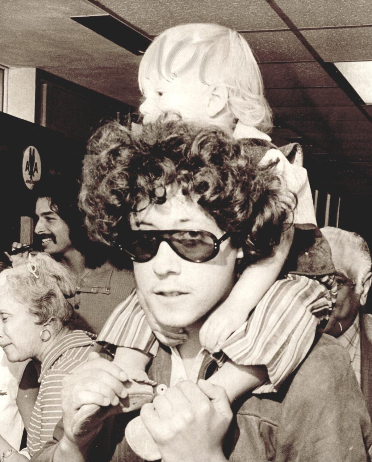 Woody Guthrie's son Arlo Guthrie carries his own son Abraham upon arrival in Oklahoma City. Arlo and his family were due to attend a benefit concert in Okemah in July 1971, where some were paying tribute to famed folk singer and songwriter Woody Guthrie, who died of Huntington's disease in 1967.
