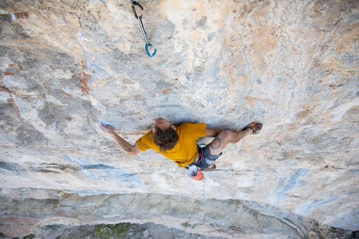 A man climbing a hard sport route in yellow shirt