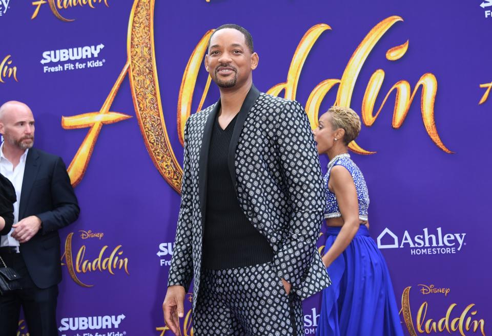 Will Smith in a patterned suit and black shirt, with Jada Pinkett Smith in a blue dress at the Aladdin premiere on the red carpet