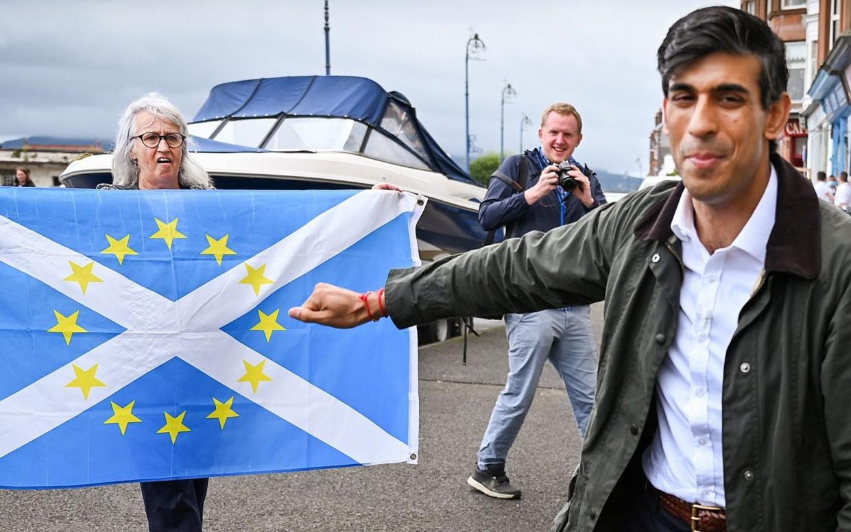 A nationalist demonstrator holds a flag as she welcomes Britain's Chancellor of the Exchequer Rishi Sunak, as he meets with local business people during a visit to Rothesay, in the Isle of Bute, Scotland, Britain, August 7, 2020. Jeff J Mitchell/Pool via REUTERS - REUTERS/REUTERS