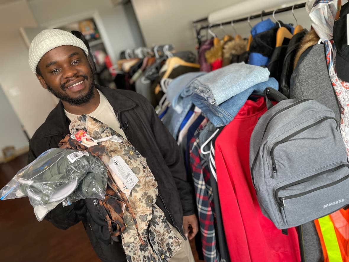 Oghosa Ogiemwonyi, co-founder of Thriftsome, an online second-hand clothing store, stands next to some of the items being sold on his website. He and his business partner, Joshua Akom, are running the business out of his Winnipeg apartment.  (Jaison Empson/CBC - image credit)