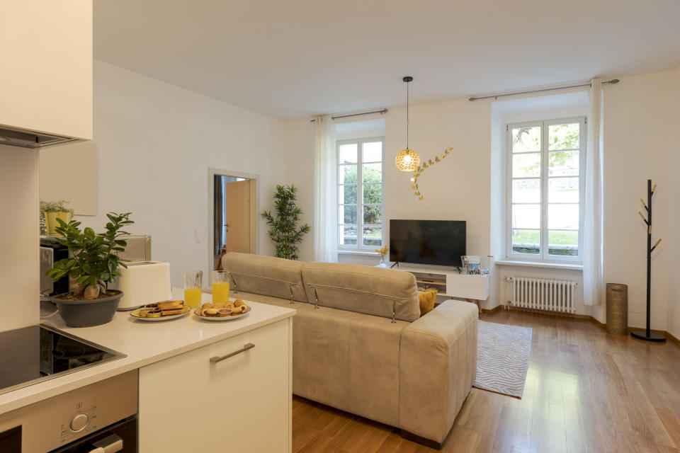 Modern living room with connected kitchen, sofa, TV, and breakfast on the table