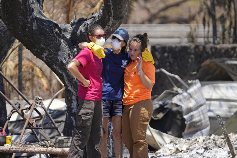 Tres mujeres se abrazan tras rebuscar entre los escombros de una vivienda destrozada por un incendio, el 11 de agosto de 2023, en Lahaina, Hawai. (AP Foto/Rick Bowmer)