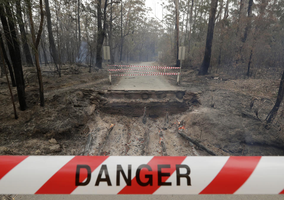 Timbers from a small bridge smolder after fire destroyed the crossing near Burrill Lake, Australia, Sunday, Jan. 5, 2020. Milder temperatures Sunday brought hope of a respite from wildfires that have ravaged three Australian states, destroying almost 2,000 homes. (AP Photo/Rick Rycroft)