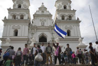 Honduran migrants stand outside a Catholic church, one waving his nation's flag, before starting to walk again as part of a caravan of hundreds of Honduran migrants making their way the U.S. in Esquipulas, Guatemala, early Tuesday, Oct. 16, 2018. U.S. President Donald Trump threatened on Tuesday to cut aid to Honduras if it doesn’t stop the impromptu caravan of migrants, but it remains unclear if governments in the region can summon the political will to physically halt the determined border-crossers. (AP Photo/Moises Castillo)