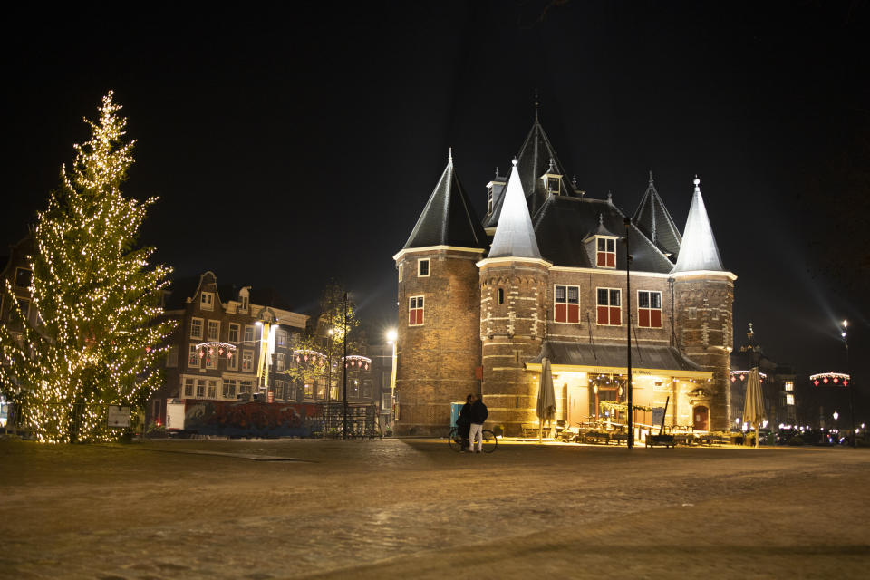 FILE- In this Thursday Dec. 31, 2020, file photo, A couple kisses on the near-deserted Nieuwmarkt square in Amsterdam, Netherlands, Thursday, Dec. 31, 2020. The Dutch government said Wednesday, Jan. 20, 2021, that it wants to impose a curfew as part of beefed-up restrictions to rein in the spread of new more contagious variants of the coronavirus that already accounts for at least one in every 10 Dutch infections.(AP Photo/Peter Dejong, File)